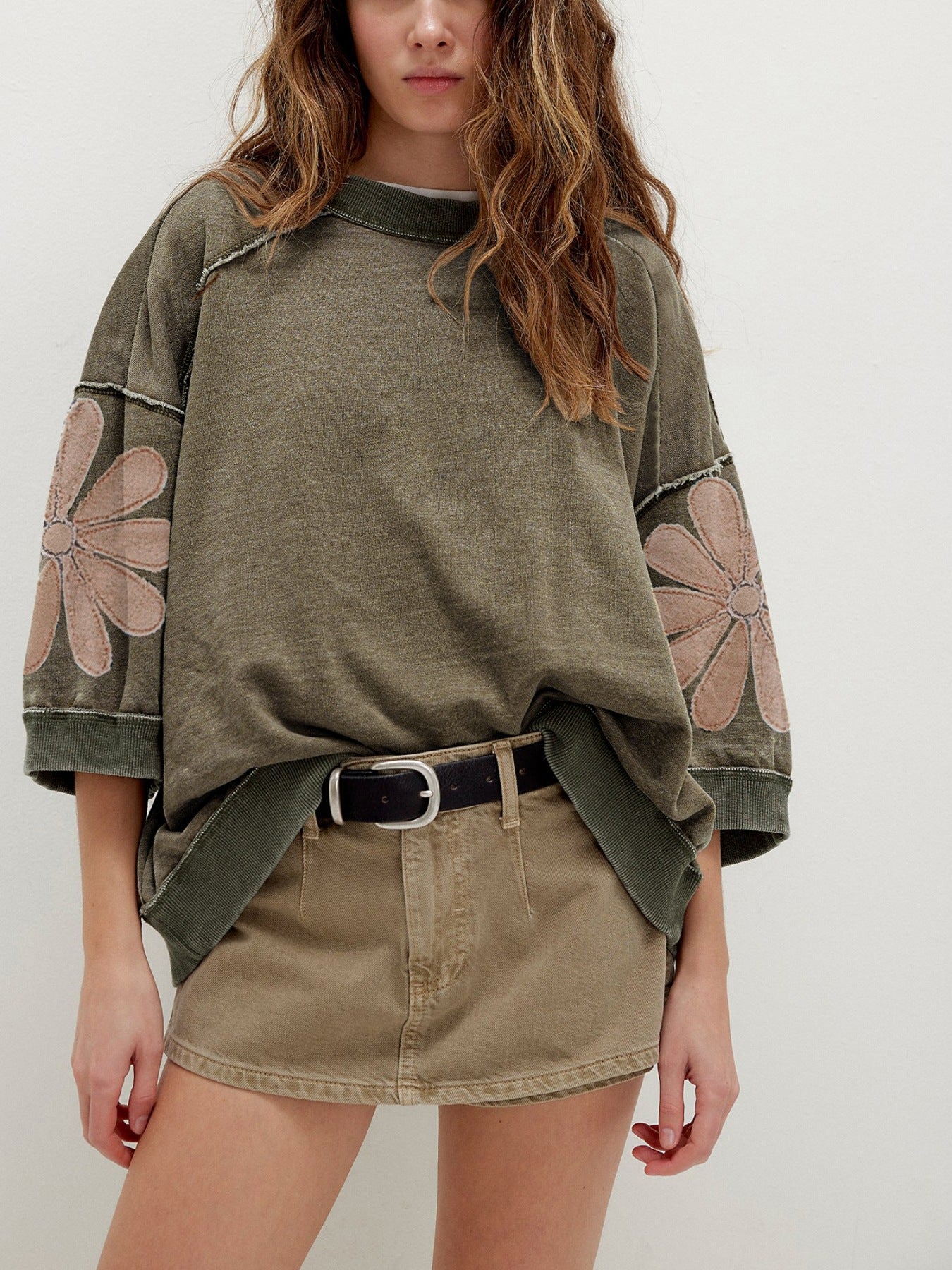 Person wearing an olive green sweatshirt with floral patterns on a plain background