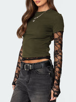 Woman wearing an olive green crop top with sheer sleeves and high-waisted dark jeans on a white background