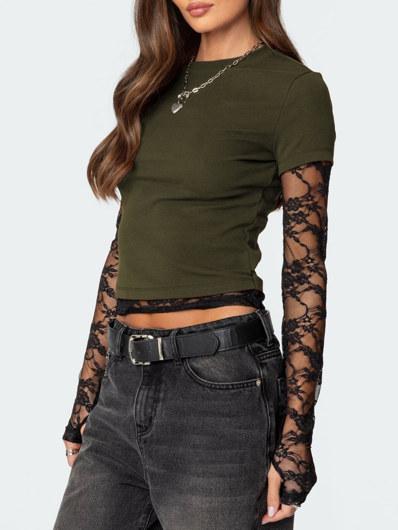 Woman wearing an olive green crop top with sheer sleeves and high-waisted dark jeans on a white background