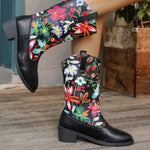 Black knee-high boots with colorful floral embroidery on a wooden floor.