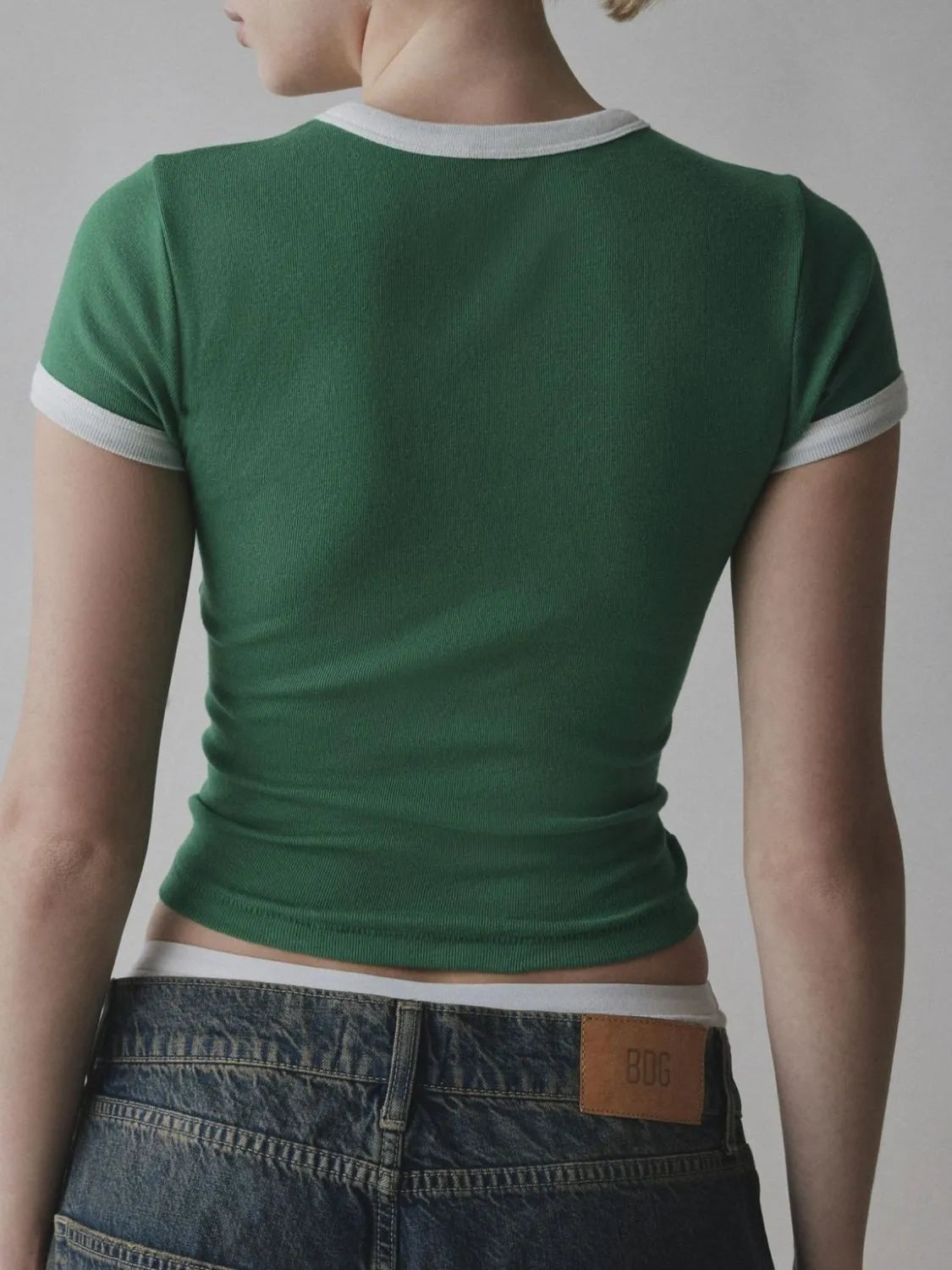 Green t-shirt with white trim worn by a person, back view, on a plain background
