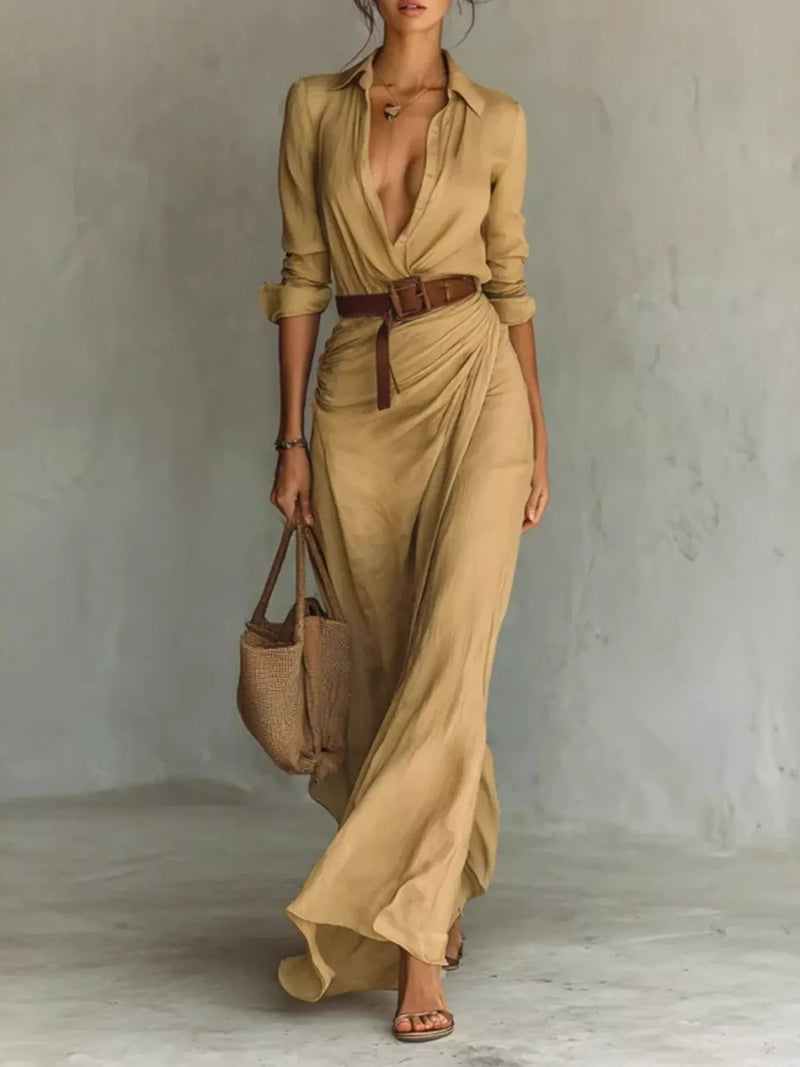 Woman wearing a beige dress with a belt, holding a matching handbag against a plain background