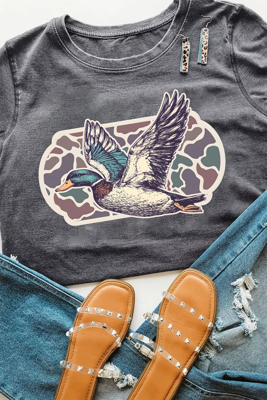 Dark gray t-shirt with a duck graphic on a denim surface with studded shoes.