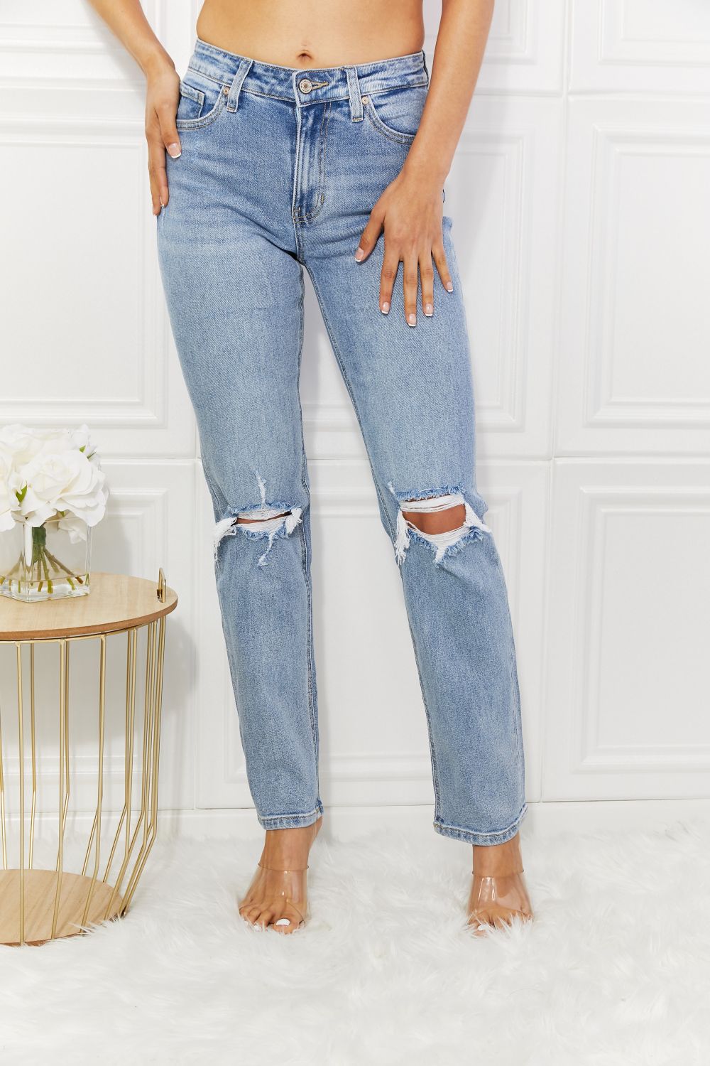 Person wearing light blue ripped jeans standing against a white wall.