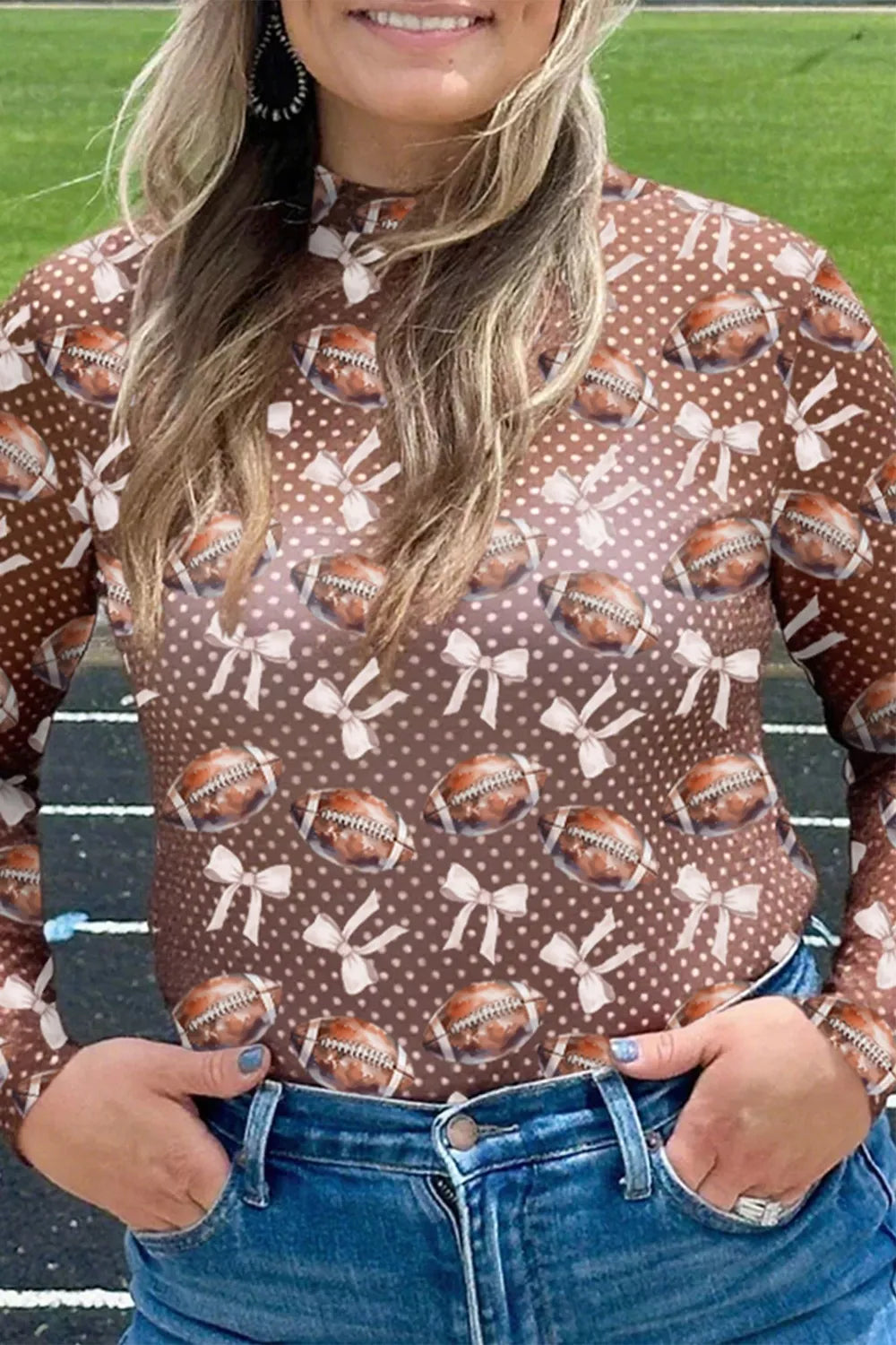 Person wearing a brown shirt with football and bow pattern on a sports field.