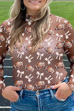 Person wearing a brown shirt with football and bow pattern on a sports field.