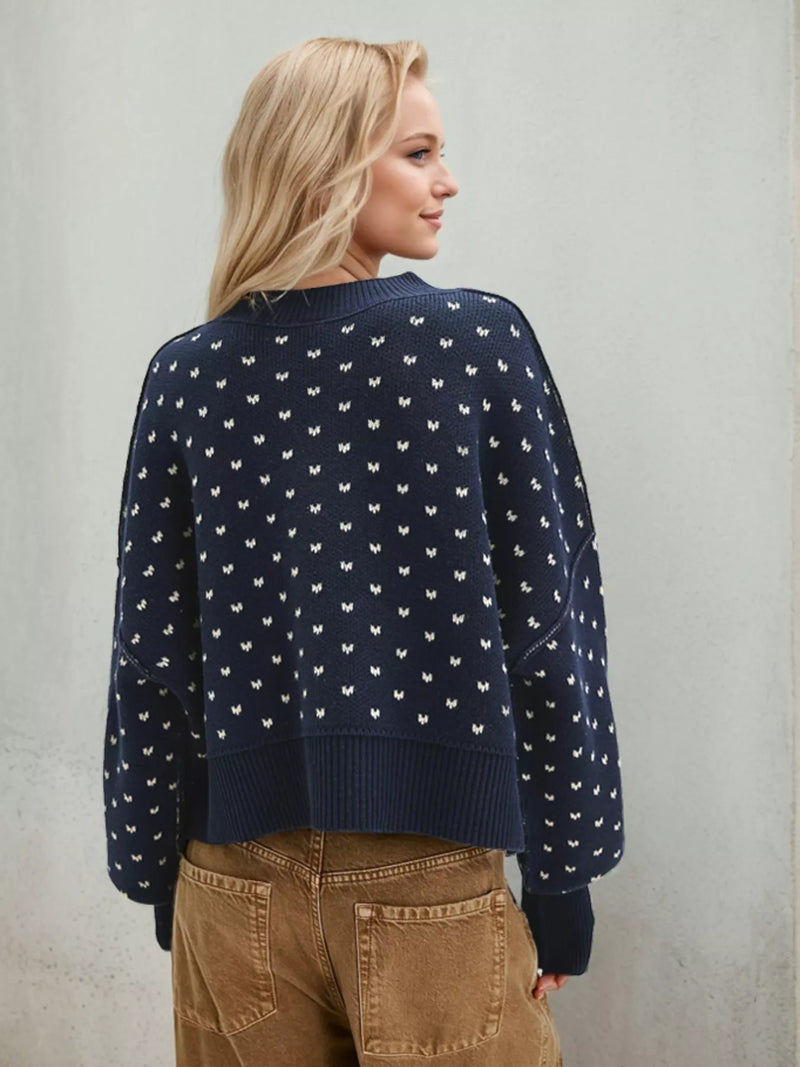 Woman wearing a navy blue sweater with white patterns against a plain background