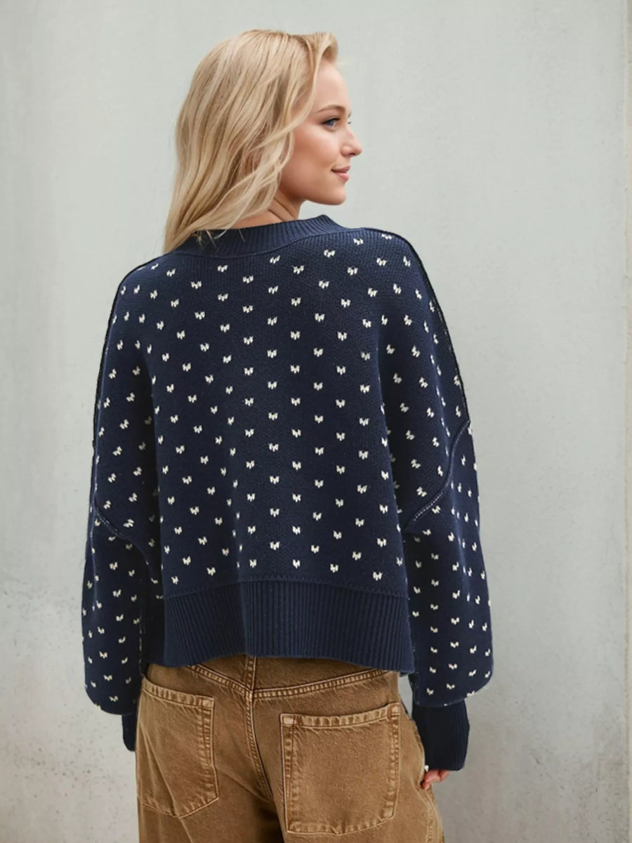 Woman wearing a navy blue sweater with white patterns against a plain background