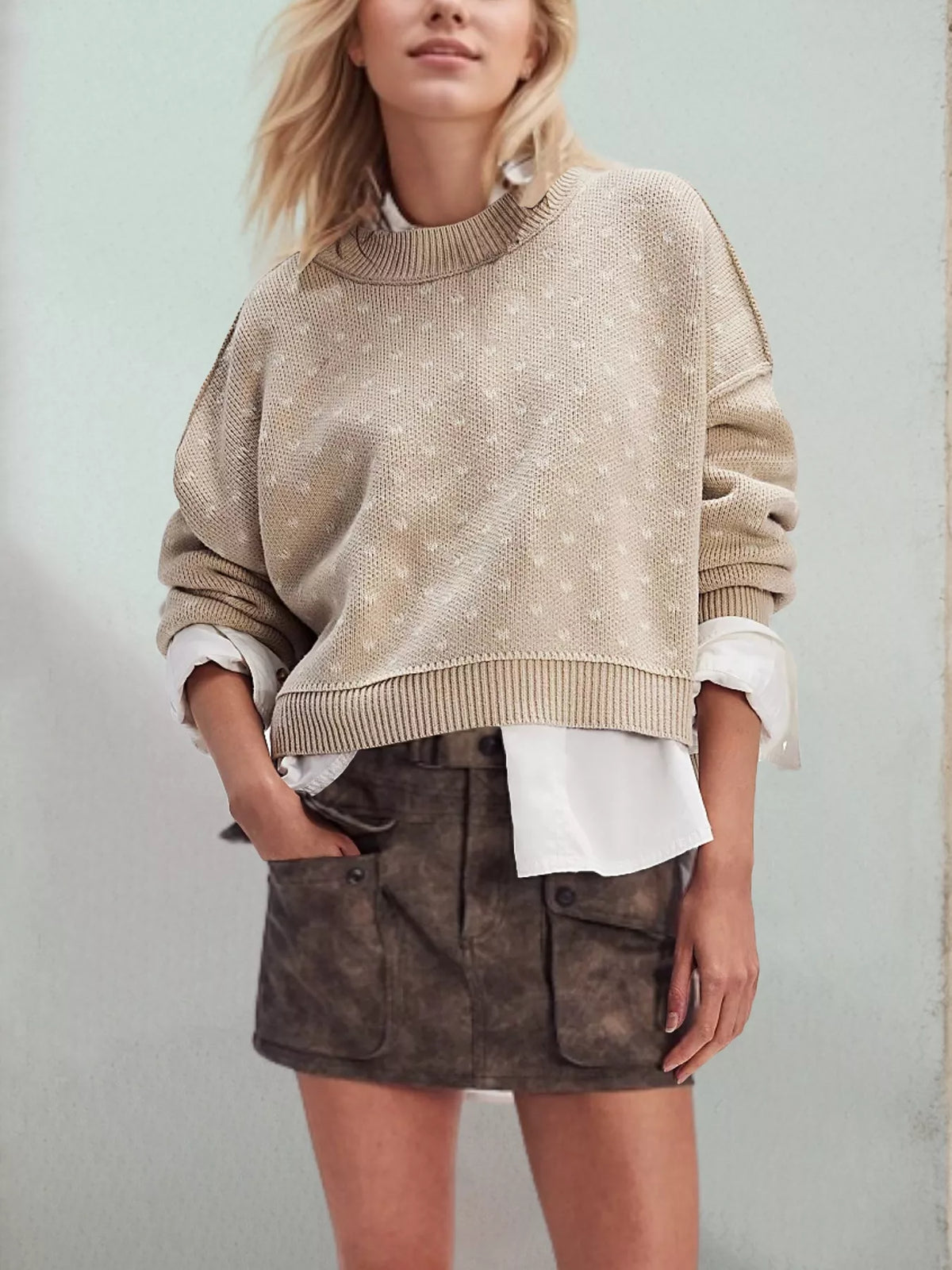 Woman wearing a beige sweater over a white shirt with a brown suede skirt against a light background
