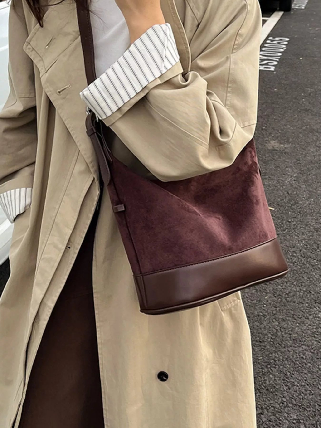 Person wearing a beige coat holding a brown handbag on a street.