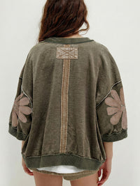 Person wearing a green sweater with floral patterns on a white background