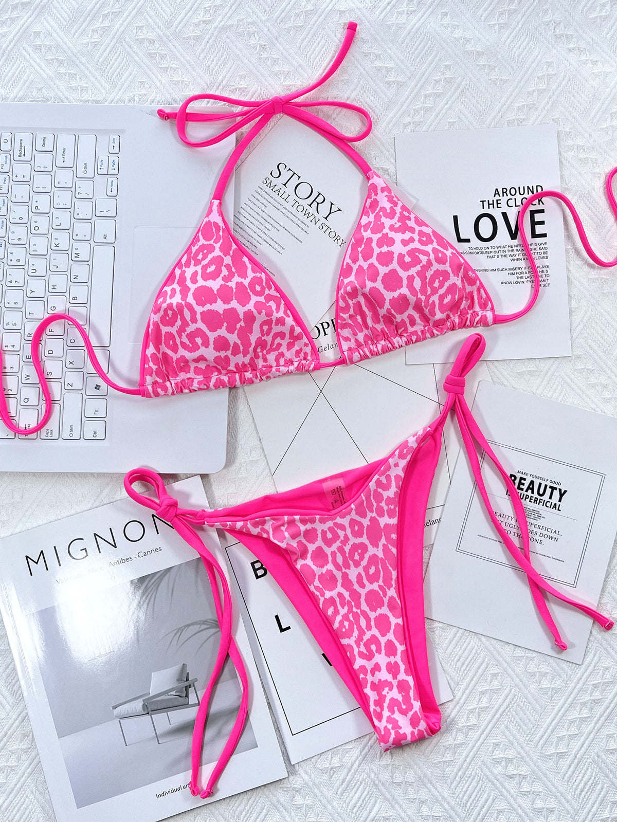 Pink leopard print bikini on a textured surface with magazines underneath