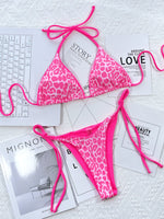 Pink leopard print bikini on a textured surface with magazines underneath