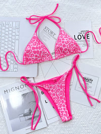 Pink leopard print bikini on a textured surface with magazines underneath