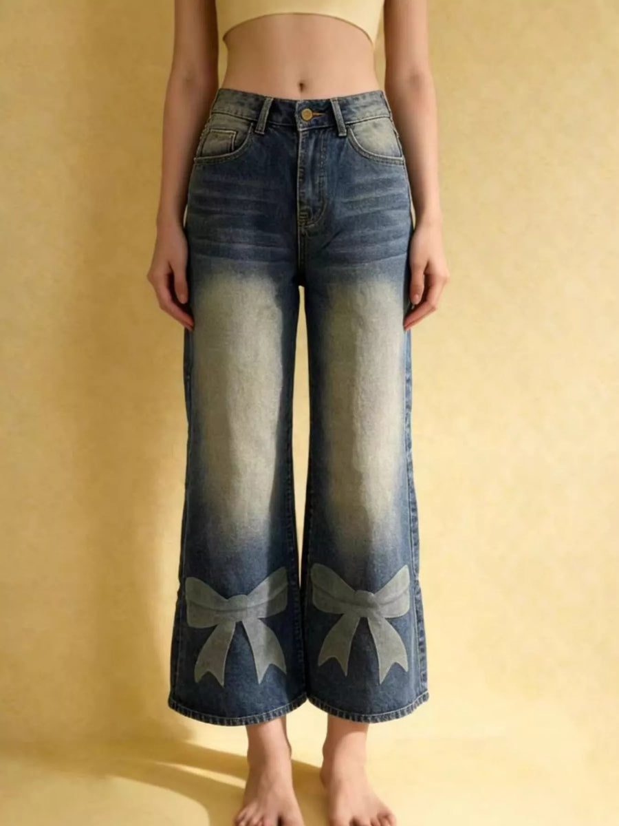 Person wearing blue jeans with bow designs on a yellow background