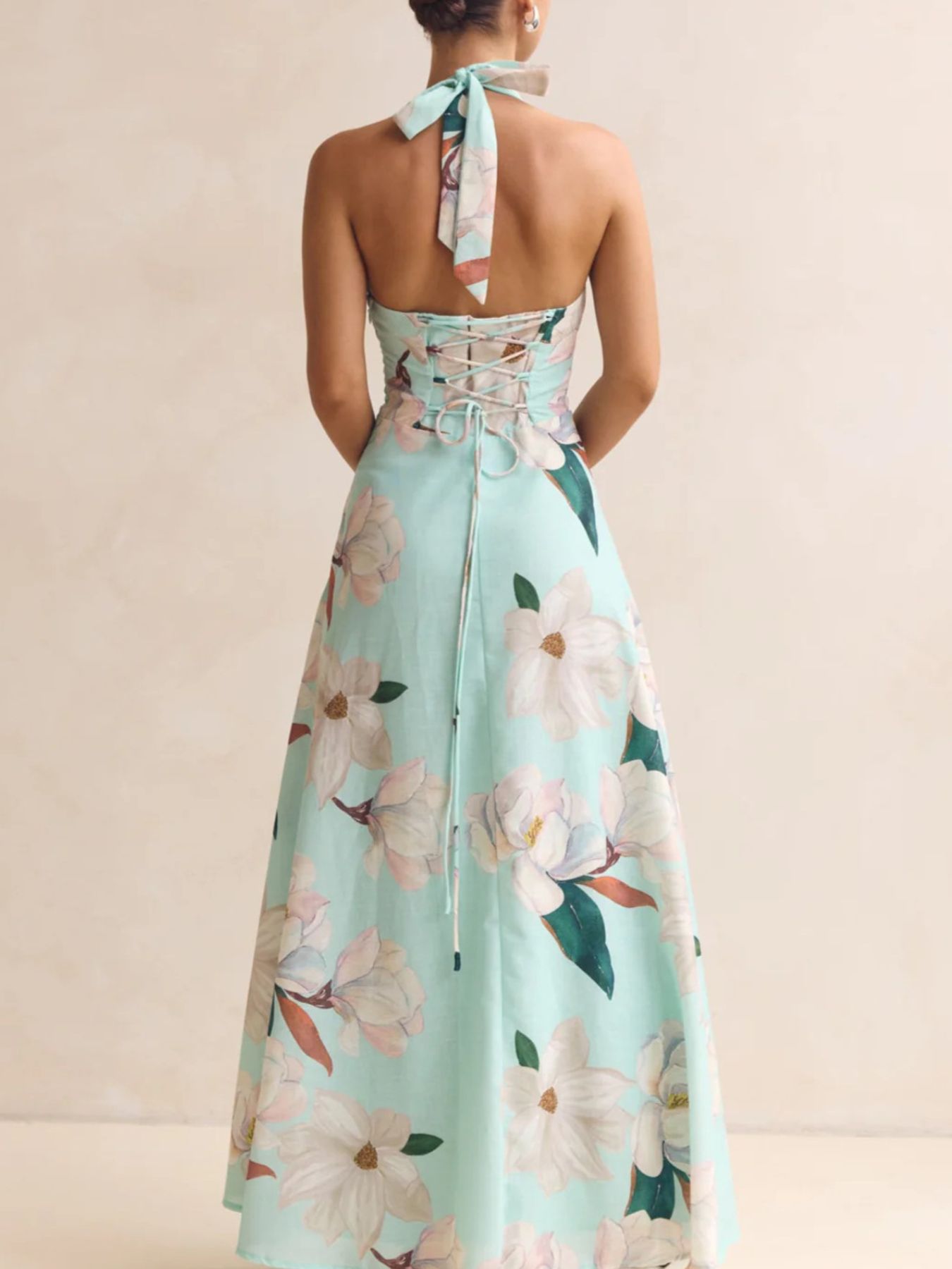 Mint green floral dress with a halter neck and tied straps on a beige background
