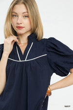 Woman wearing a navy blue dress with white trim on a white background