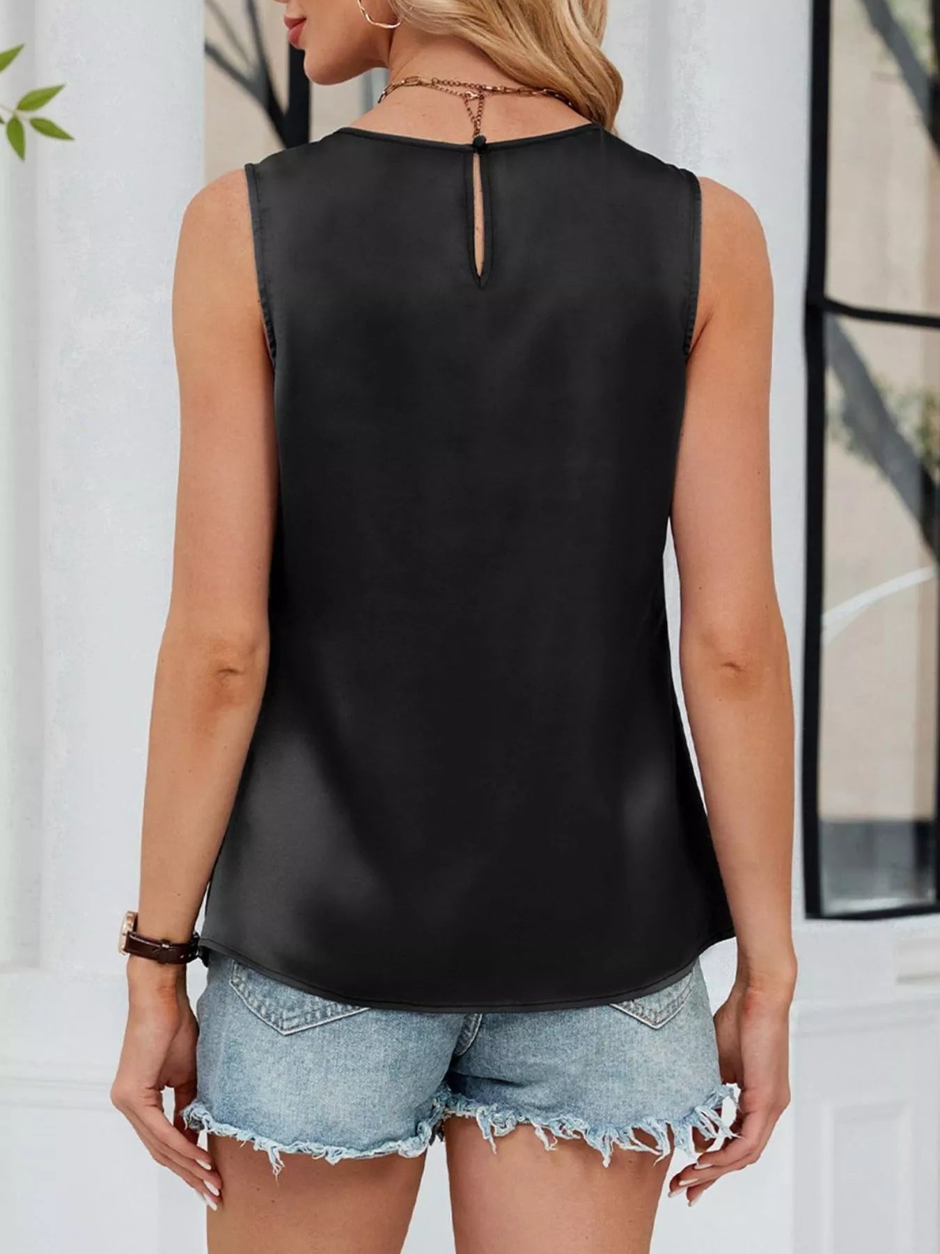 Woman wearing a black sleeveless top and denim shorts outdoors.