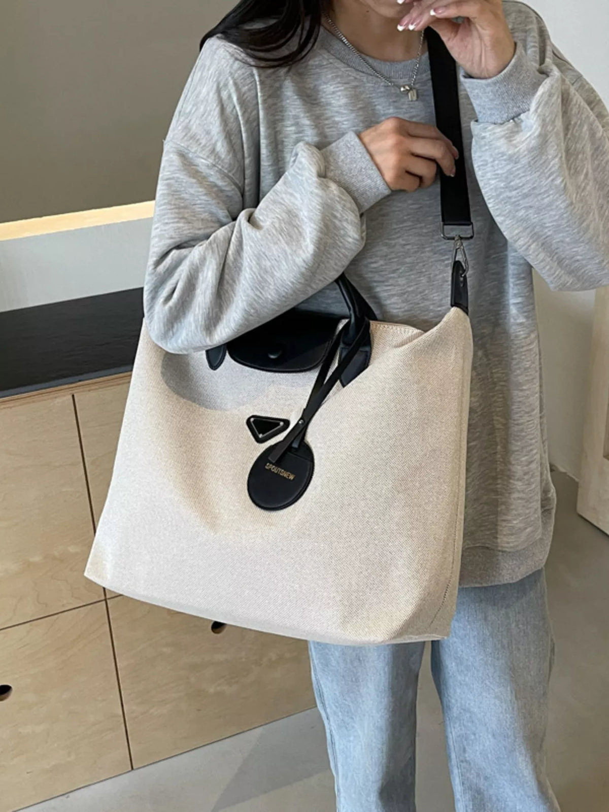 Person holding a beige tote bag with black accents indoors.