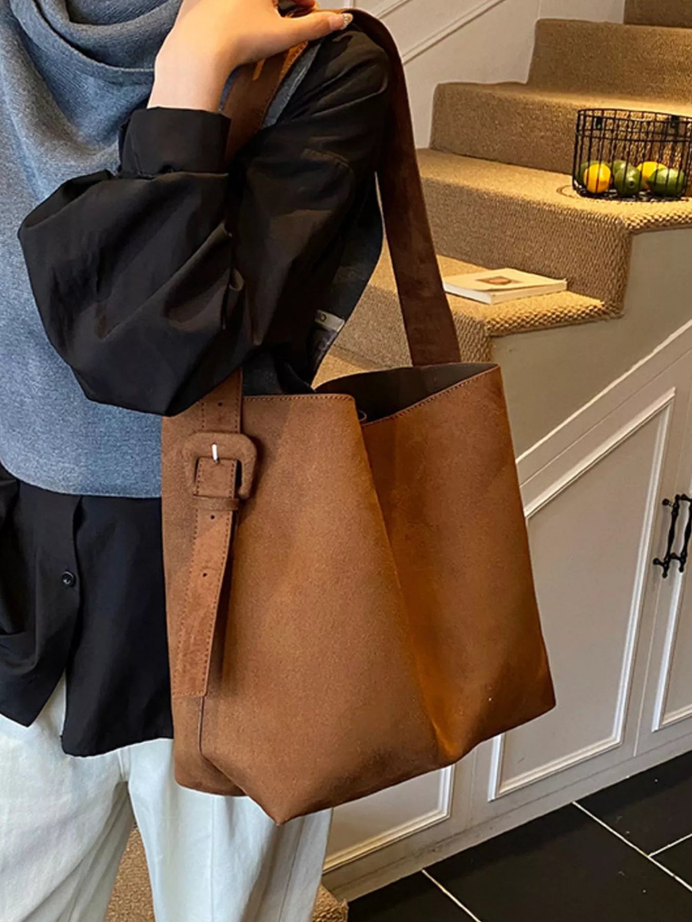 Person holding a brown leather bag in a home setting