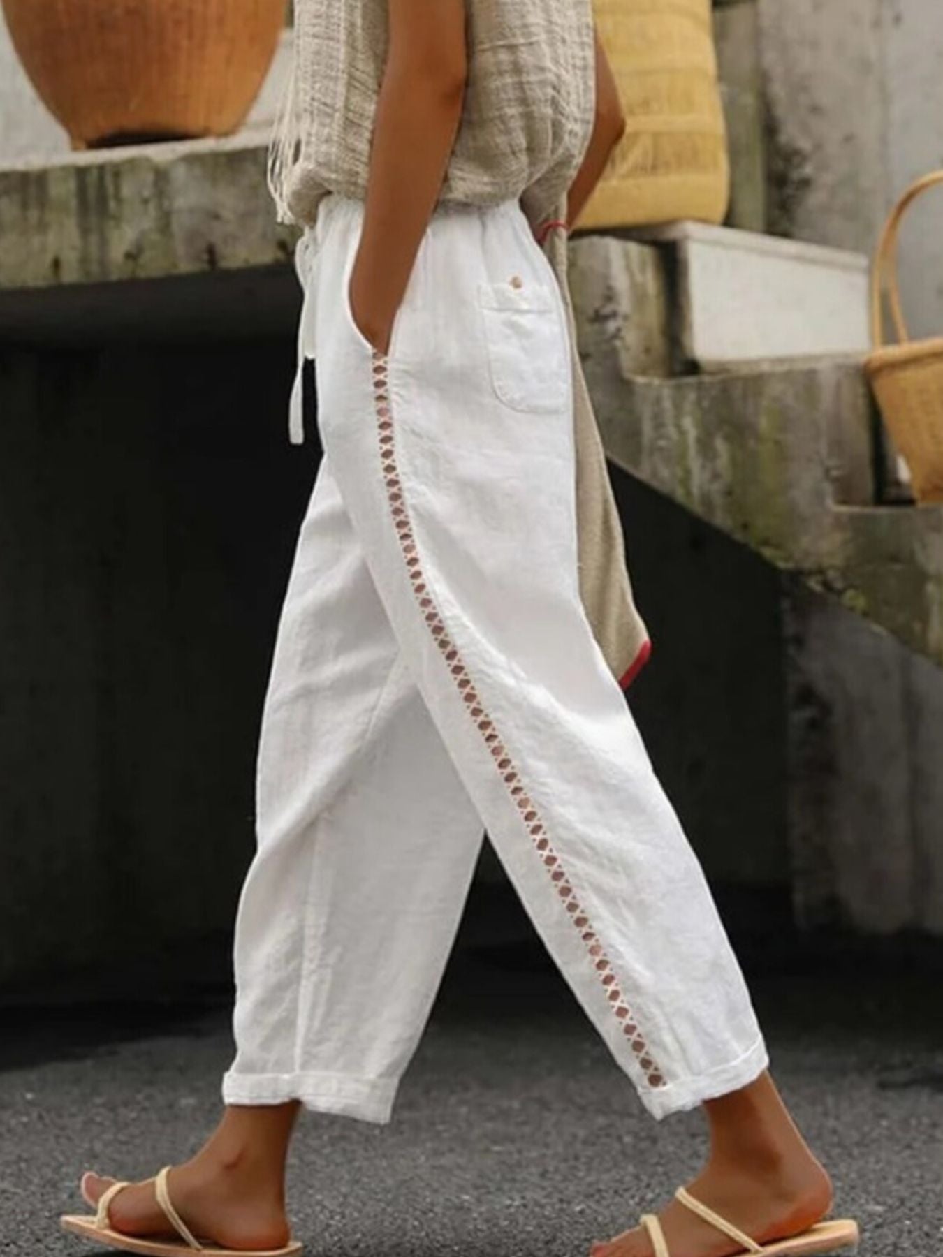 Person wearing white pants with brown embroidery details outdoors.