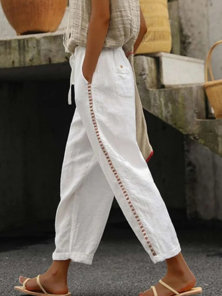 Person wearing white pants with brown embroidery details outdoors.