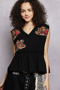 Woman wearing a black sleeveless top with floral embroidery on a gray background