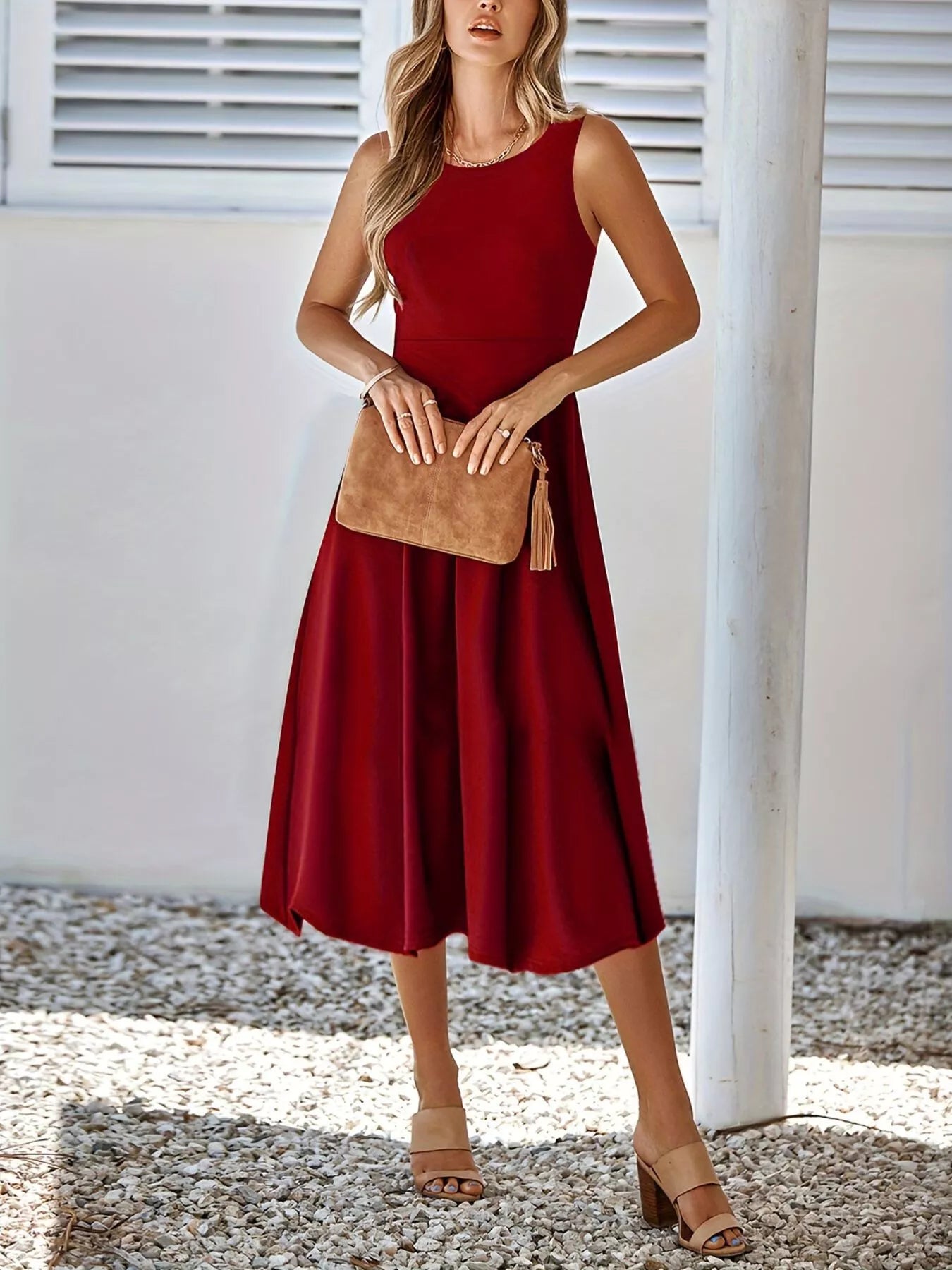 Woman wearing a red dress holding a brown clutch against a white wall.