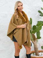 Woman wearing a brown poncho with fur trim against a white wall.