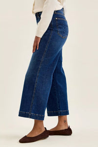 Person wearing blue jeans and a white top on a beige background