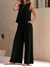 Person wearing a black sleeveless top and wide-leg pants against a beige wall.