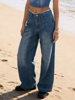 Person wearing blue jeans standing on a sandy beach.