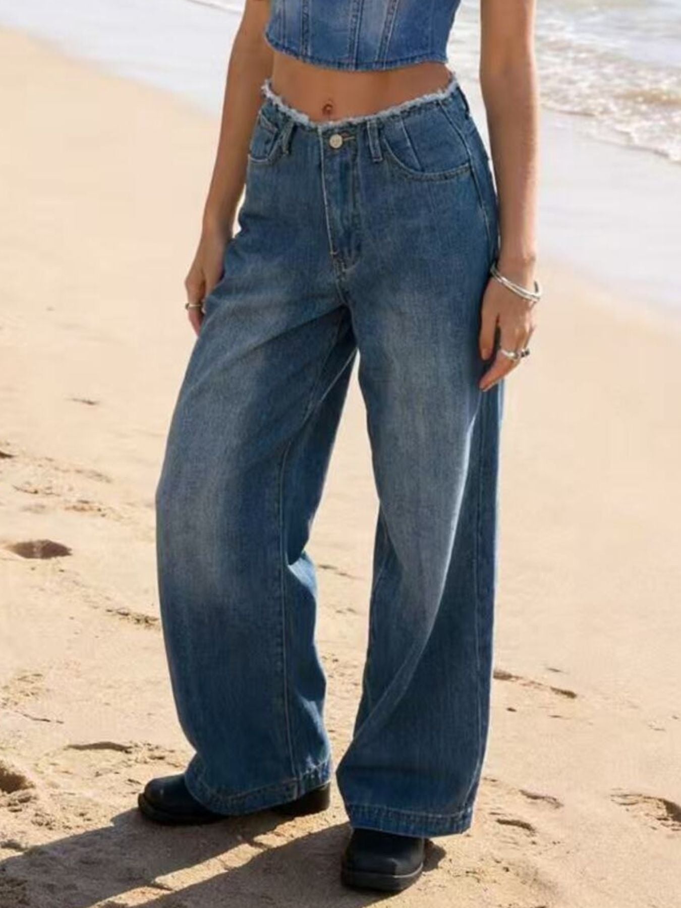 Person wearing blue jeans standing on a sandy beach.