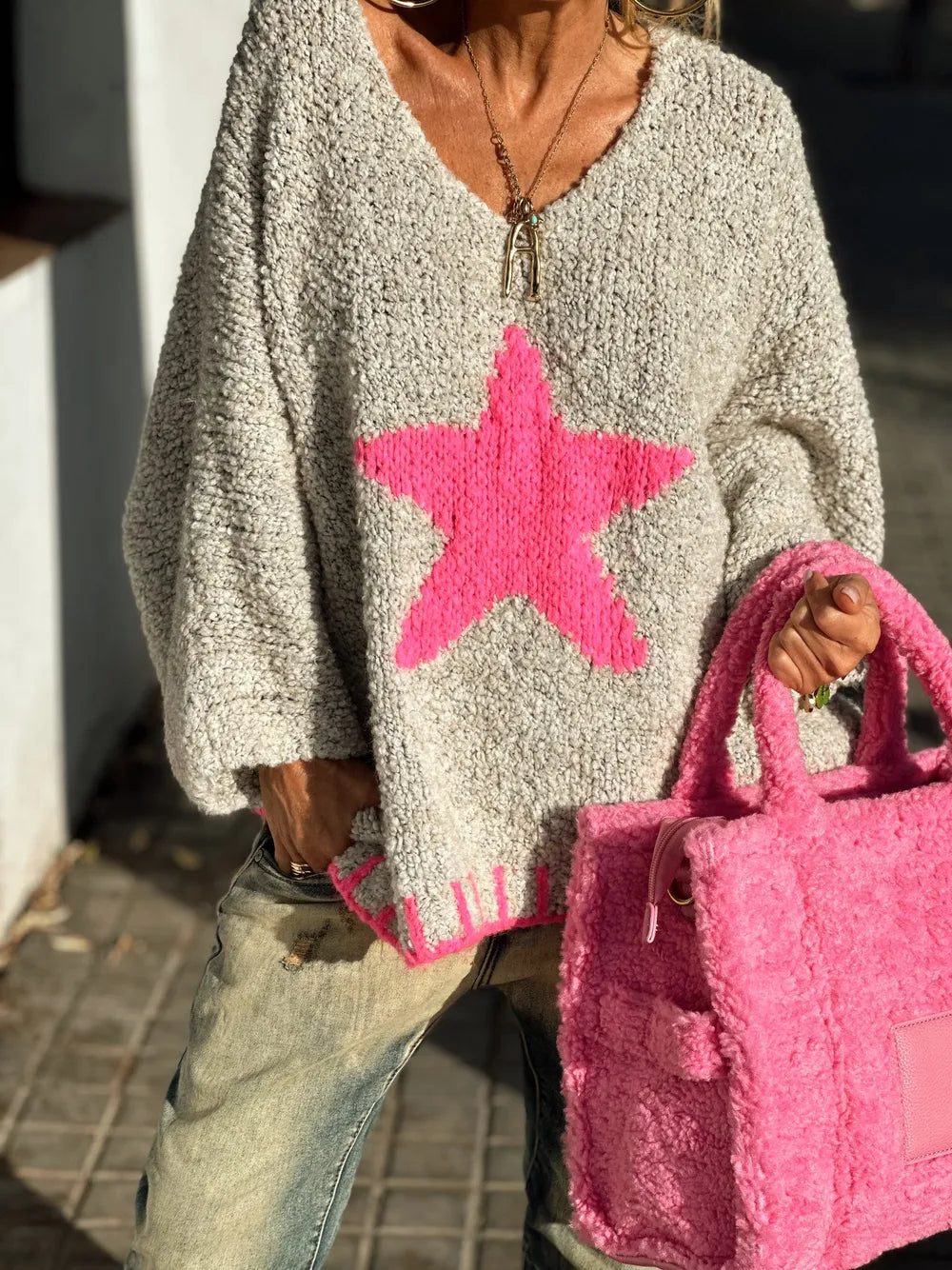 Person wearing a gray sweater with a pink star design, holding a pink bag.