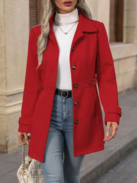 Person wearing a red coat over a white top and blue jeans, standing against a neutral background.