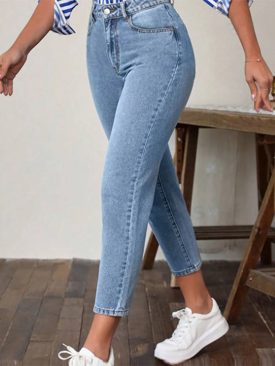 Person wearing blue jeans and white sneakers on a wooden floor.