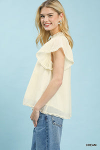 Woman wearing a cream blouse with ruffled sleeves against a light blue background