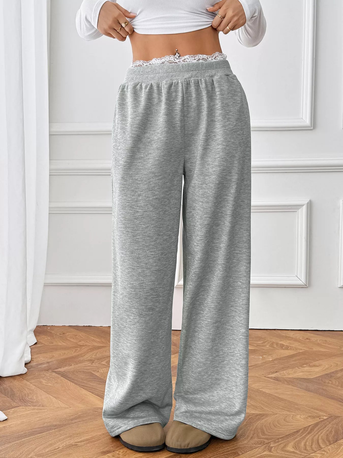 Person wearing gray sweatpants with lace waistband on a wooden floor.