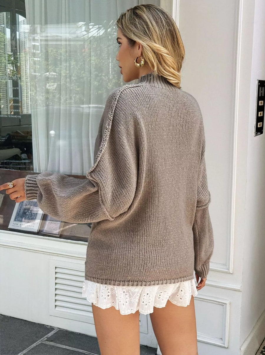 Woman wearing a brown sweater and white lace shorts in a room with a window.