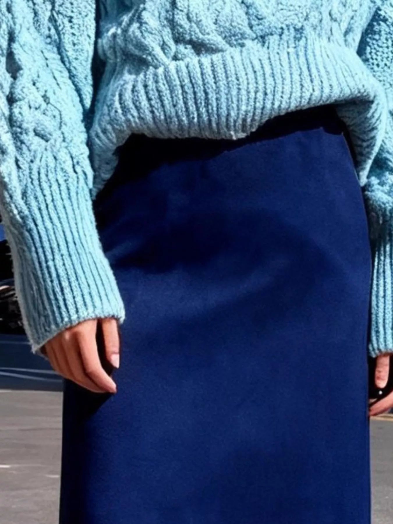 Person wearing a light blue knitted sweater and dark blue skirt.