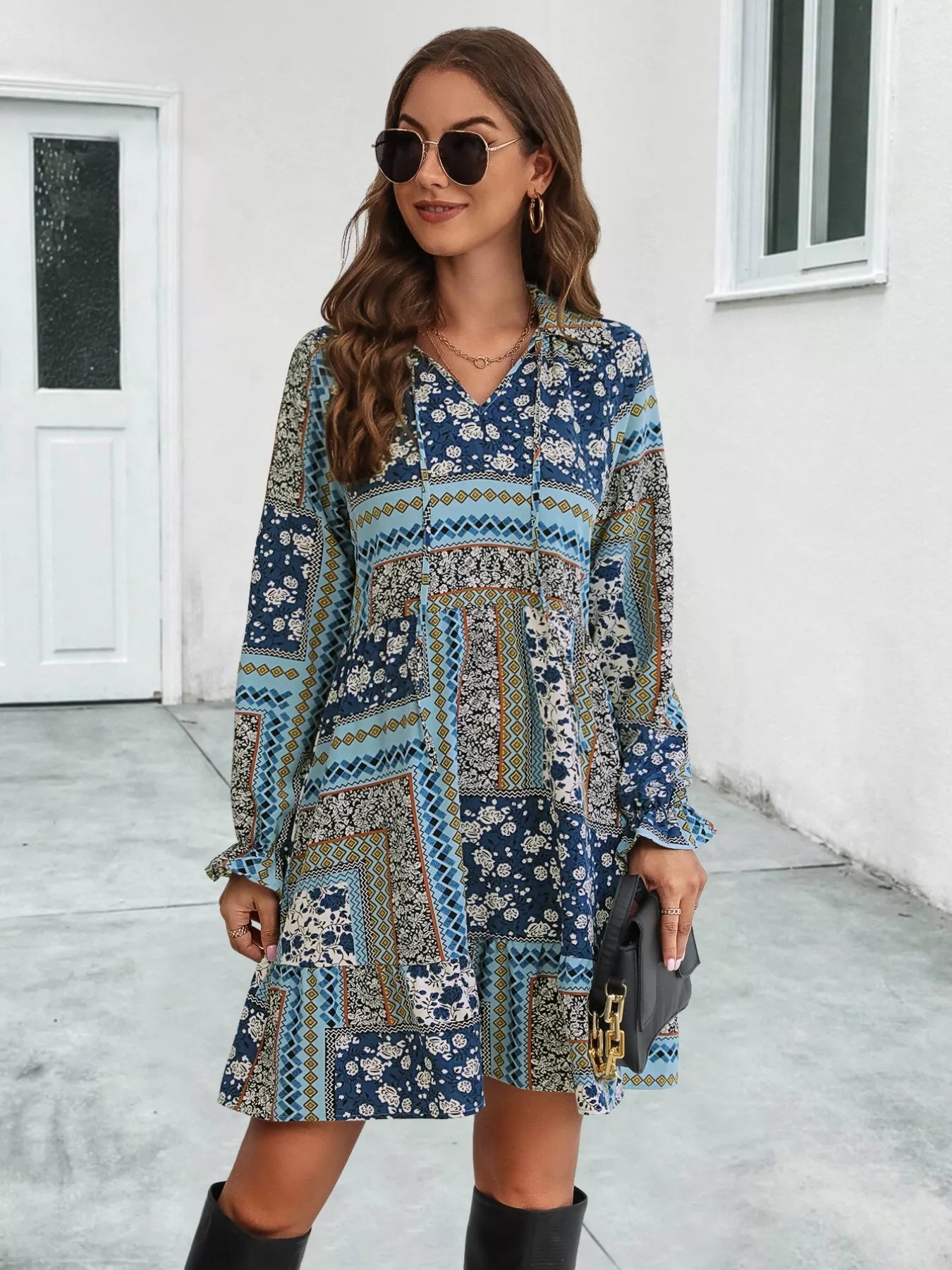 Woman wearing a patterned dress standing in front of a white wall.