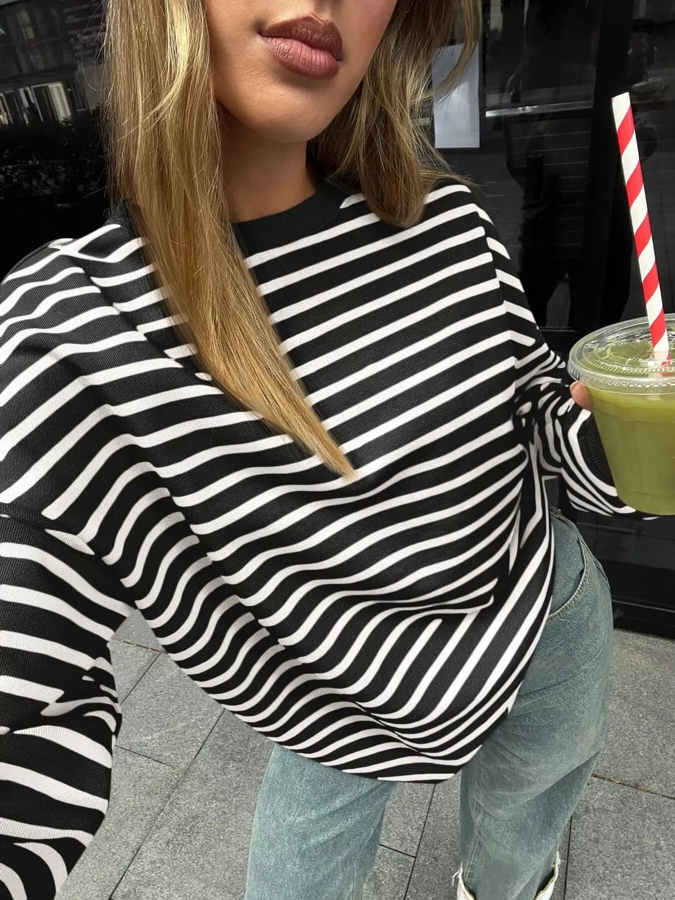 Person wearing a black and white striped sweater holding a drink with a straw.