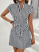 Woman wearing a black and white striped dress with a belt against a white background