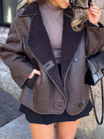 A woman wearing a brown faux-suede shearling jacket with a dark brown sherpa lining, styled with a taupe turtleneck, black skirt, and a black handbag.