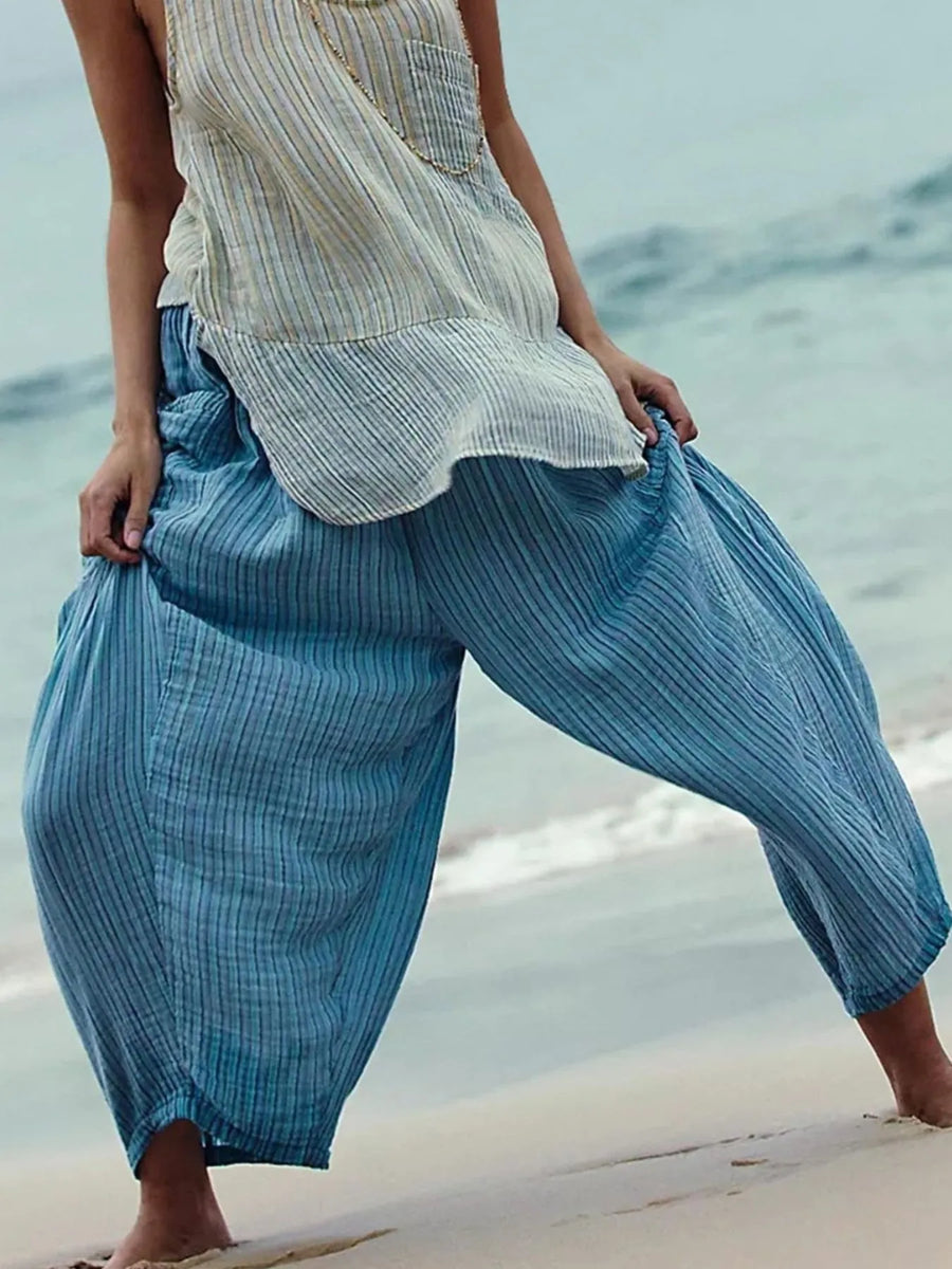 Person wearing blue striped pants and a white top on a beach.