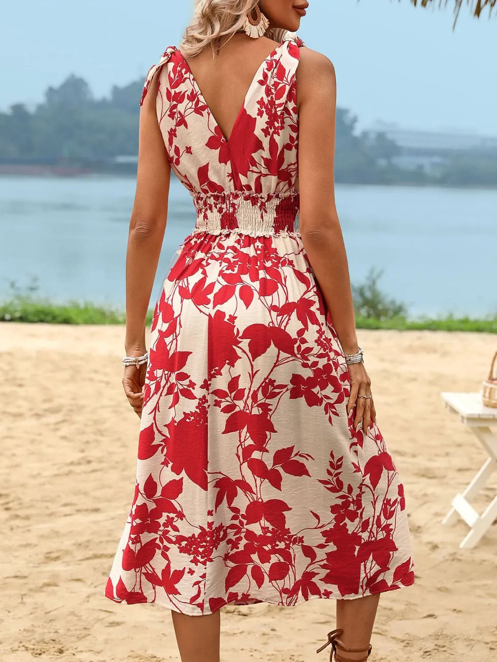 Woman wearing a red and white floral dress on a beach.