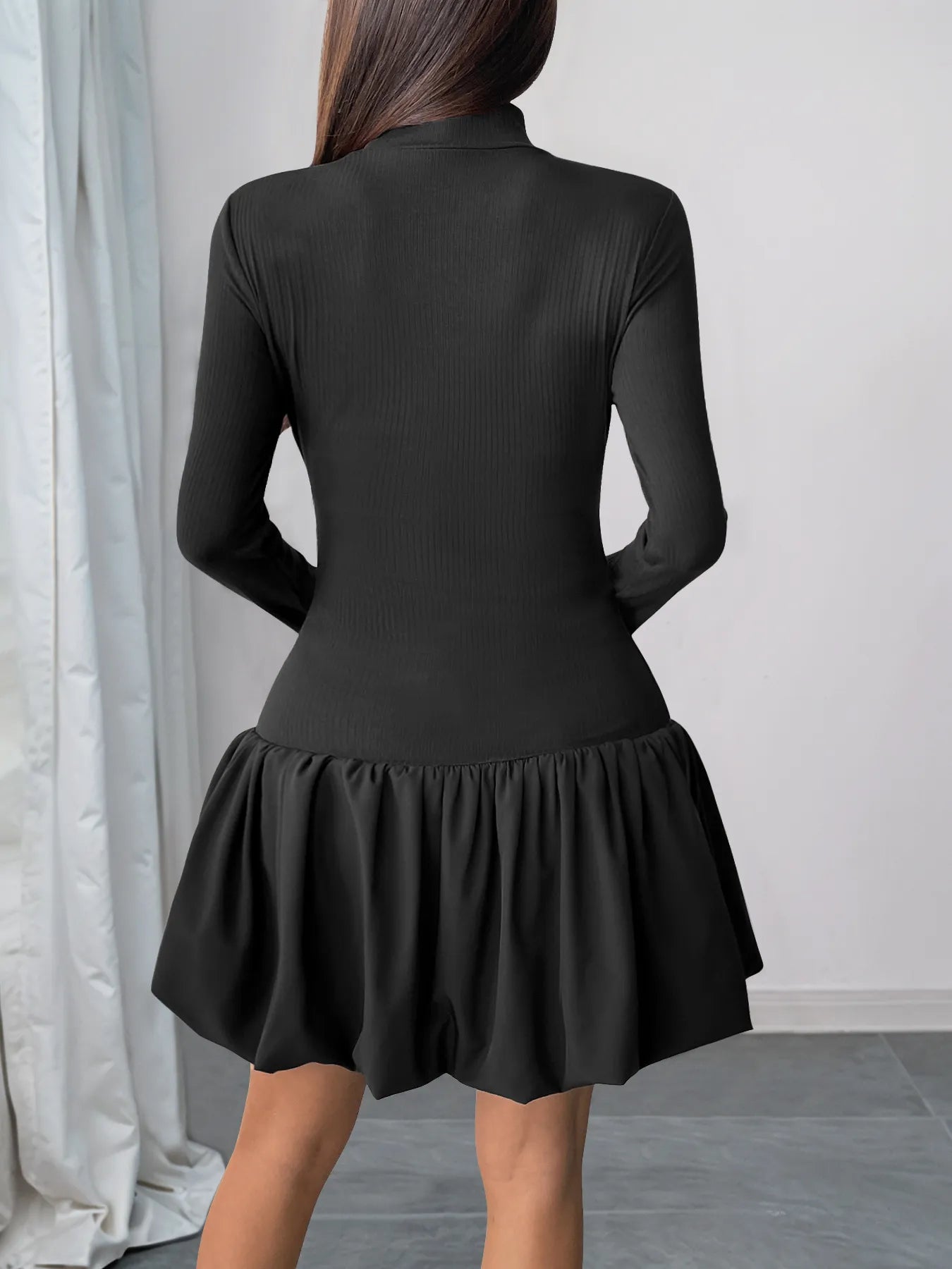 Black dress with long sleeves and a flared skirt worn by a person, against a neutral background.