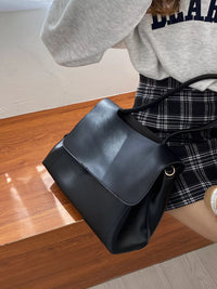 Person holding a black handbag on a wooden floor