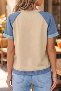 Person wearing a beige and blue baseball shirt with denim shorts in an outdoor setting.