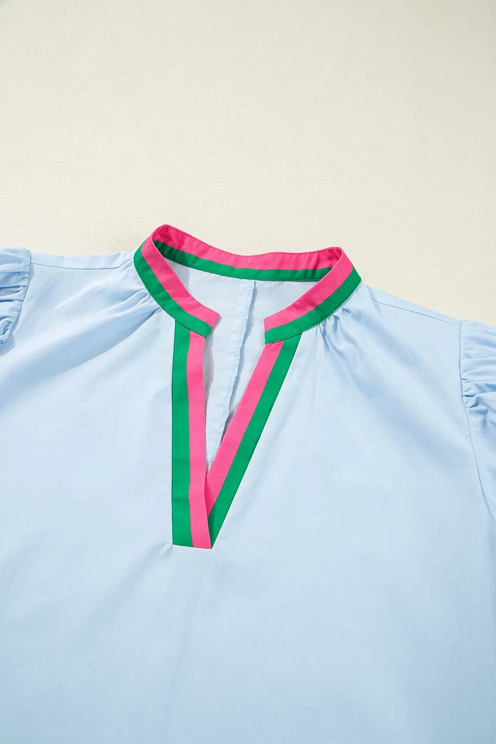 Light blue top with pink and green trim on a beige background
